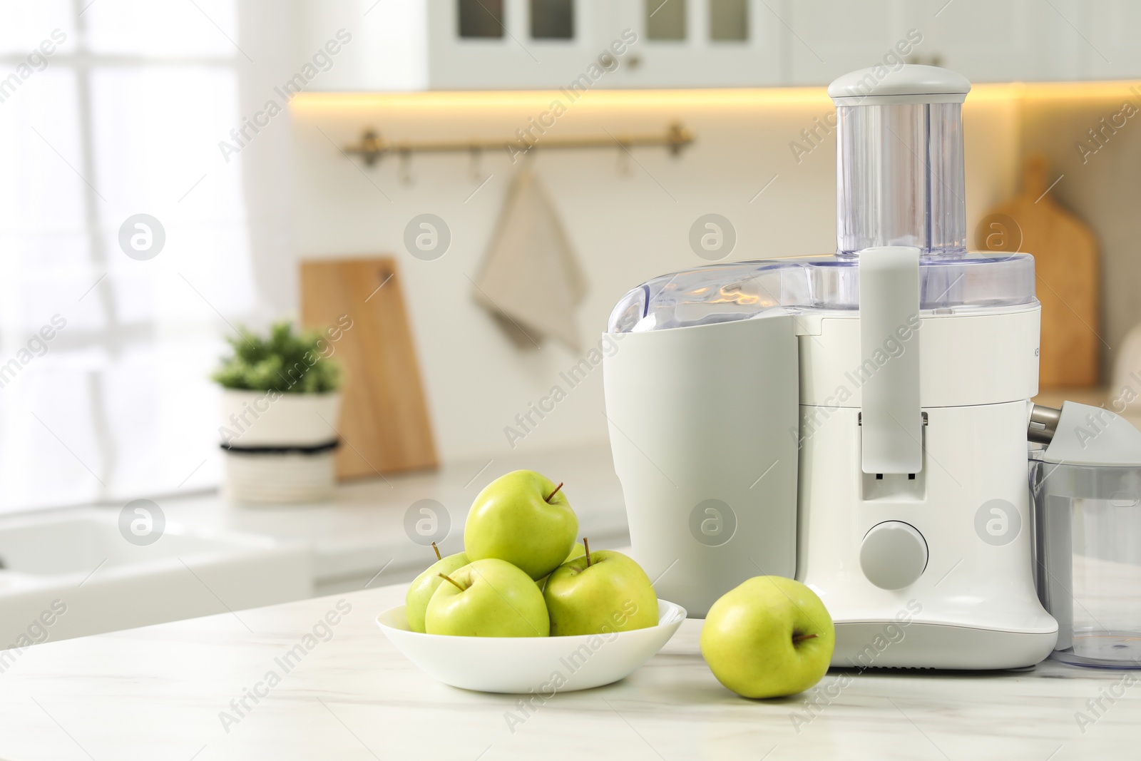 Photo of Modern juicer and apples on white marble table in kitchen, space for text