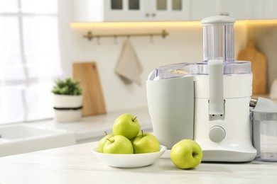 Photo of Modern juicer and apples on white marble table in kitchen, space for text