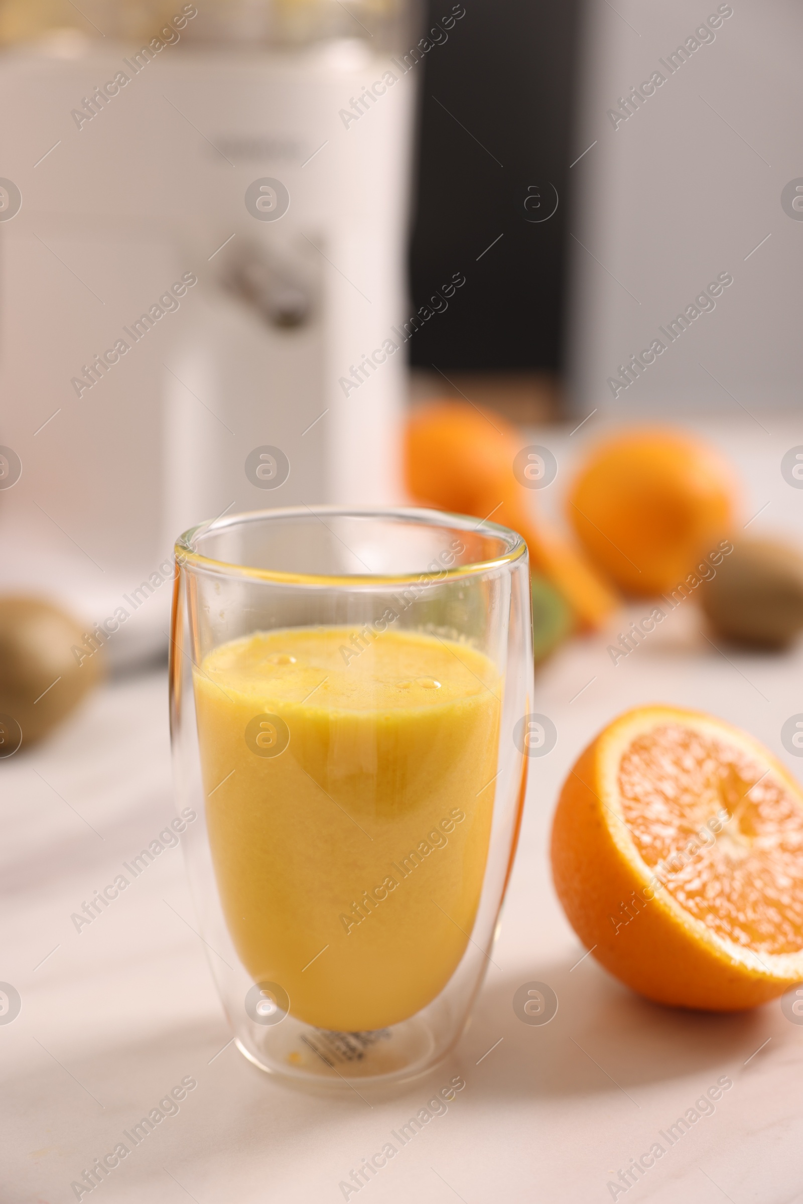 Photo of Glass of fresh juice, modern juicer and fruits on white marble table in kitchen, selective focus