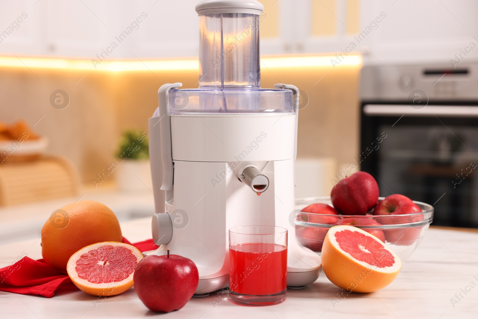 Photo of Modern juicer, fresh fruits and glass on white marble table in kitchen