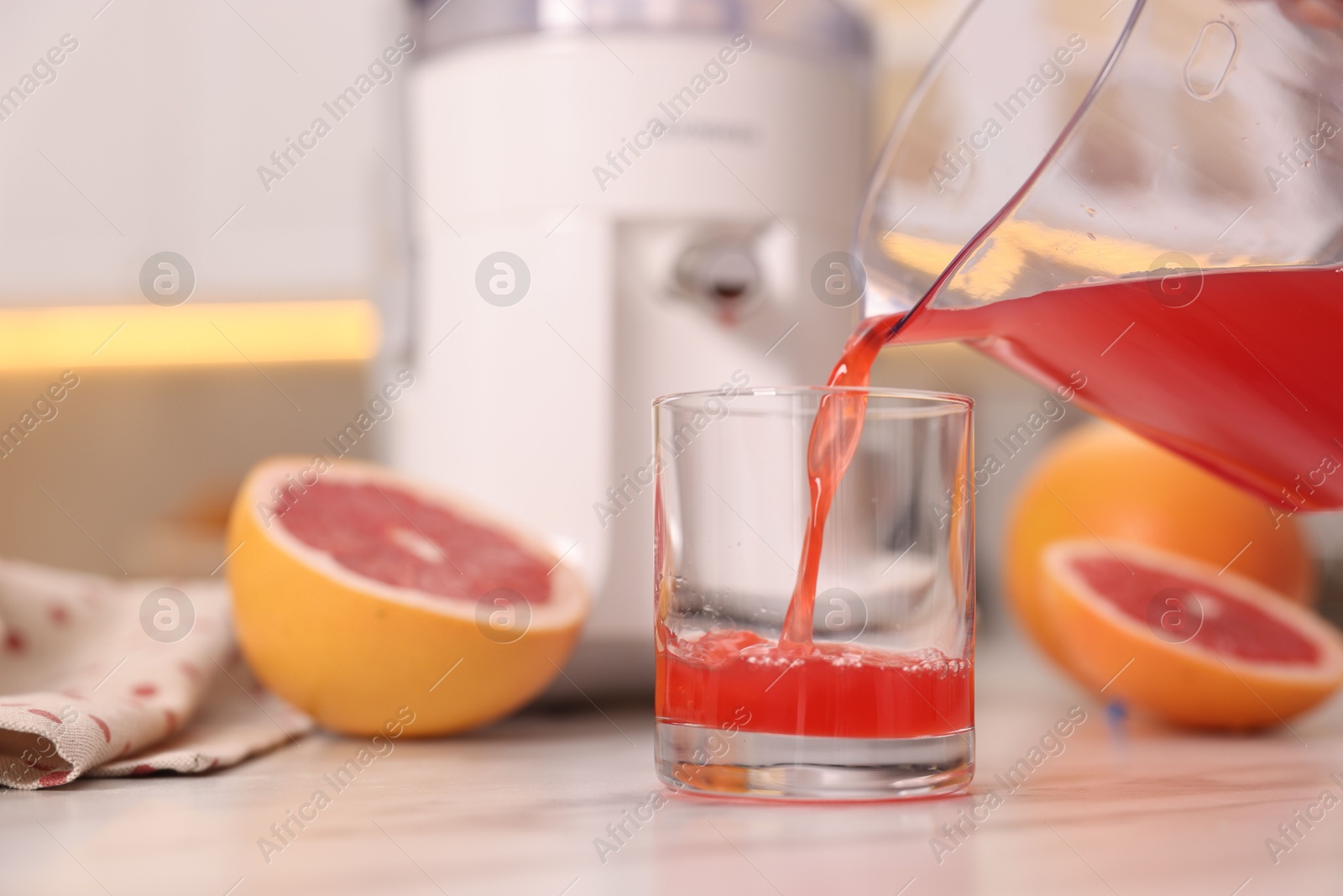 Photo of Pouring tasty grapefruit juice into glass at white marble table in kitchen, closeup