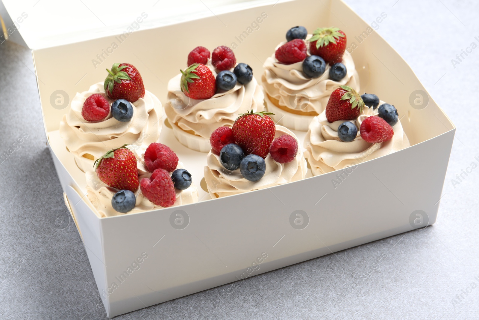 Photo of Tasty cupcakes with different berries in box on light grey table