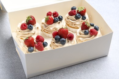 Photo of Tasty cupcakes with different berries in box on light grey table