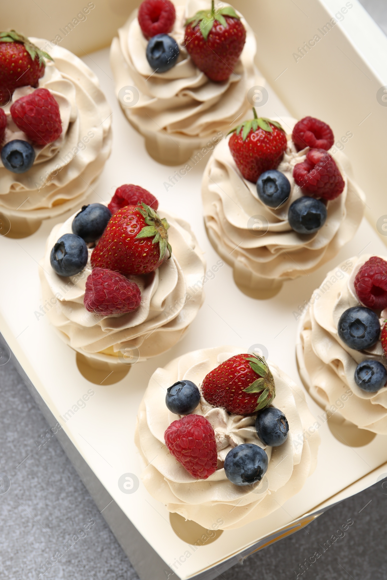 Photo of Tasty cupcakes with different berries in box on light grey table, above view