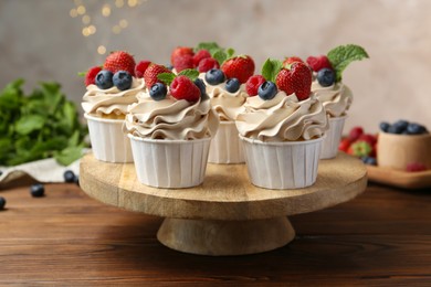 Photo of Tasty cupcakes with different berries and mint on wooden table, closeup