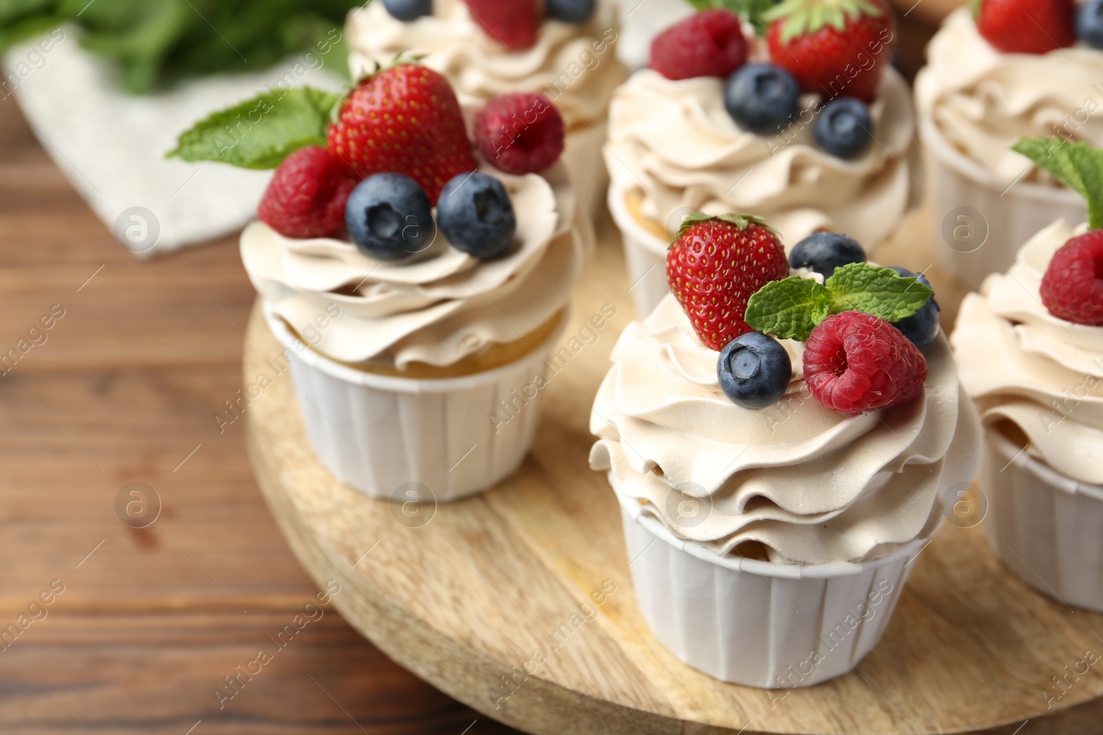 Photo of Tasty cupcakes with different berries and mint on wooden table, closeup