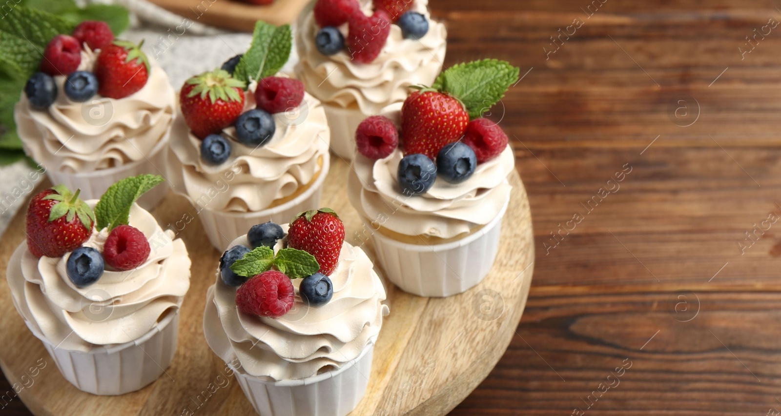 Photo of Tasty cupcakes with different berries and mint on wooden table, closeup. Space for text