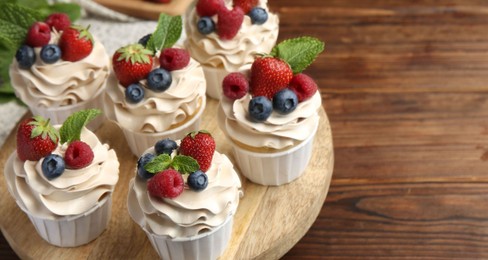 Photo of Tasty cupcakes with different berries and mint on wooden table, closeup. Space for text