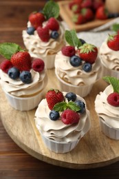 Photo of Tasty cupcakes with different berries and mint on wooden table, closeup