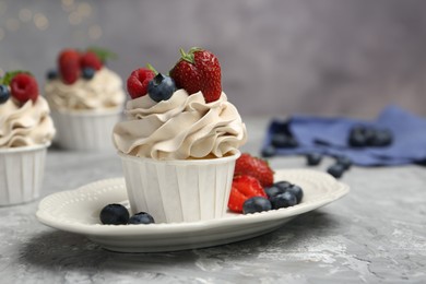 Photo of Tasty cupcakes with different berries on light grey table, closeup