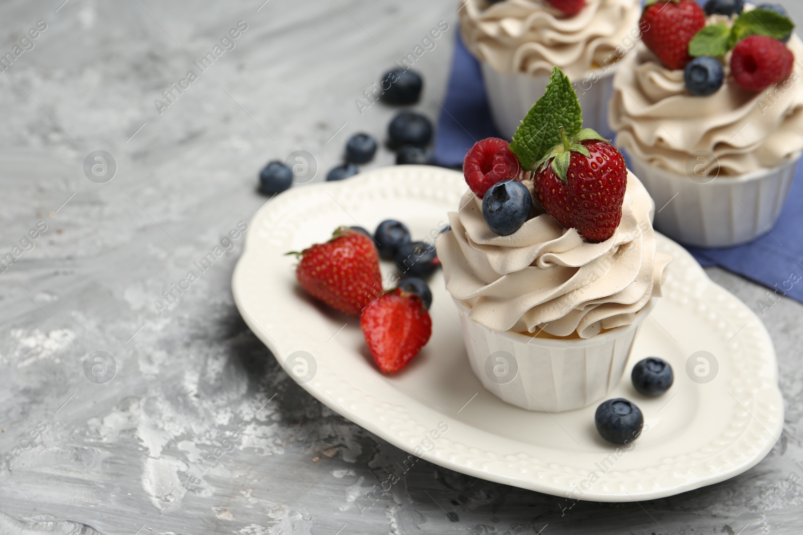 Photo of Tasty cupcakes with different berries and mint on light grey table, closeup. Space for text