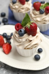 Photo of Tasty cupcakes with different berries and mint on light grey table, closeup