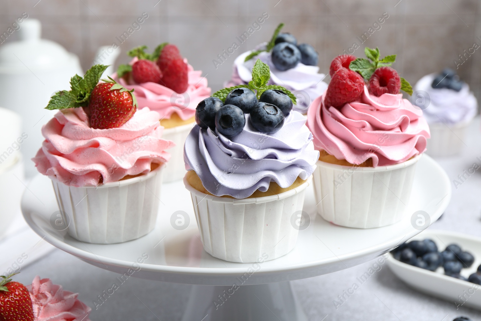 Photo of Tasty cupcakes with different berries on light grey table, closeup