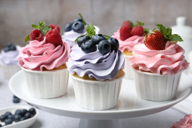 Photo of Tasty cupcakes with different berries on light grey table, closeup