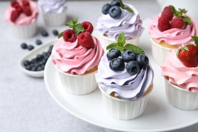 Photo of Tasty cupcakes with different berries on light grey table, closeup