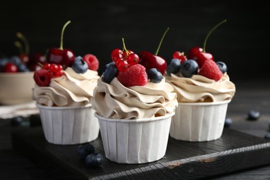 Photo of Tasty cupcakes with different berries on black wooden table, closeup