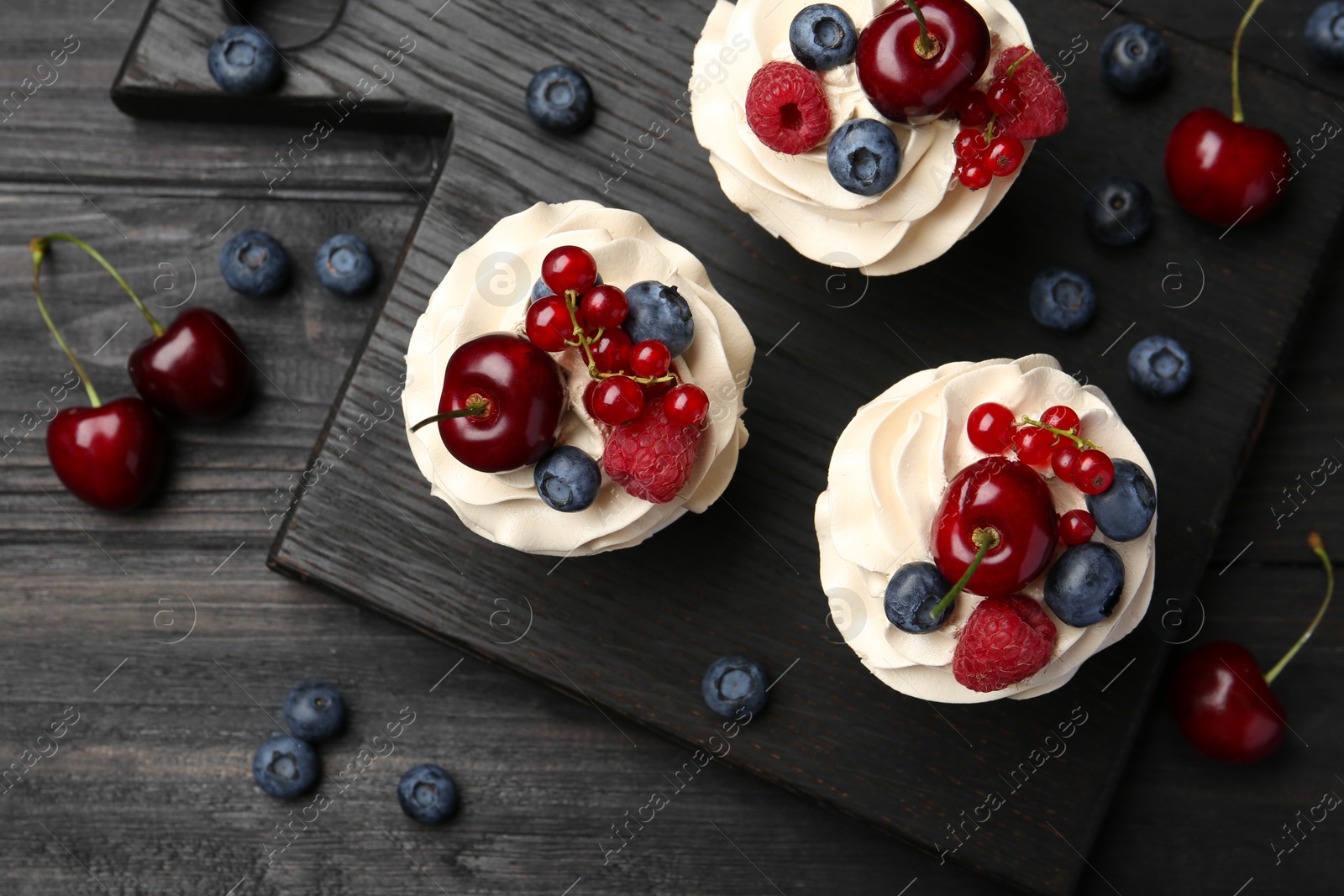 Photo of Tasty cupcakes with different berries on black wooden table, flat lay