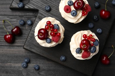 Photo of Tasty cupcakes with different berries on black wooden table, flat lay