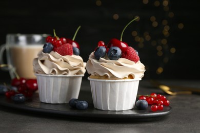 Photo of Tasty cupcakes with different berries on grey table, closeup