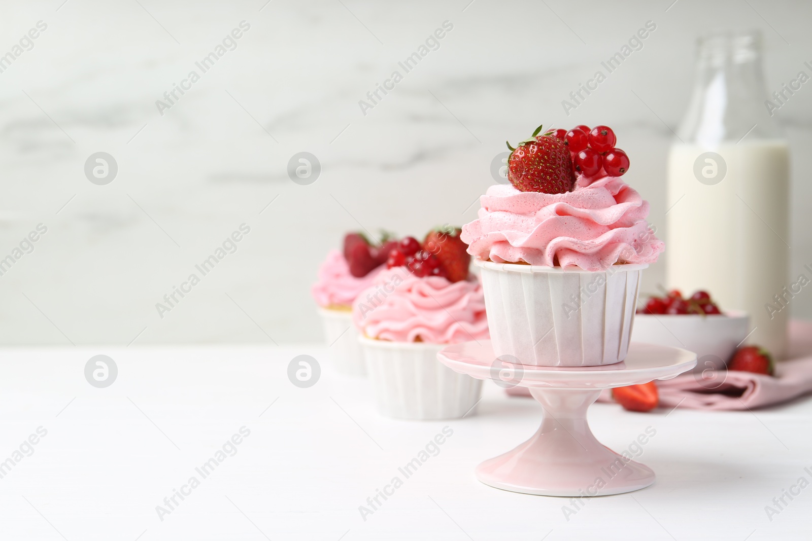 Photo of Tasty cupcakes with strawberries and red currants on white table, space for text