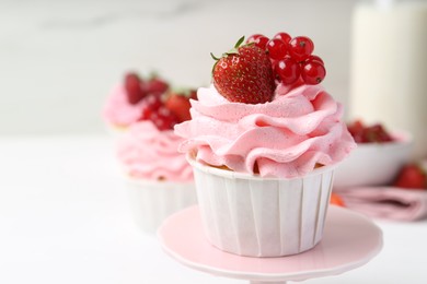 Photo of Tasty cupcake with strawberries and red currants on white table, closeup. Space for text