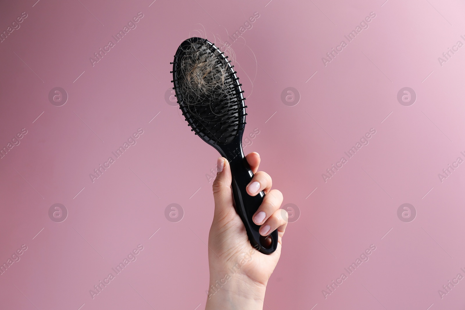 Photo of Woman holding brush with lost hair on pink background, closeup