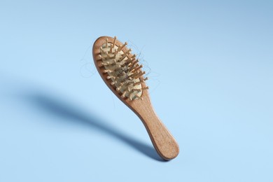 Photo of Wooden brush with lost hair in air on light blue background