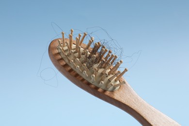 Photo of Wooden brush with lost hair in air on light blue background