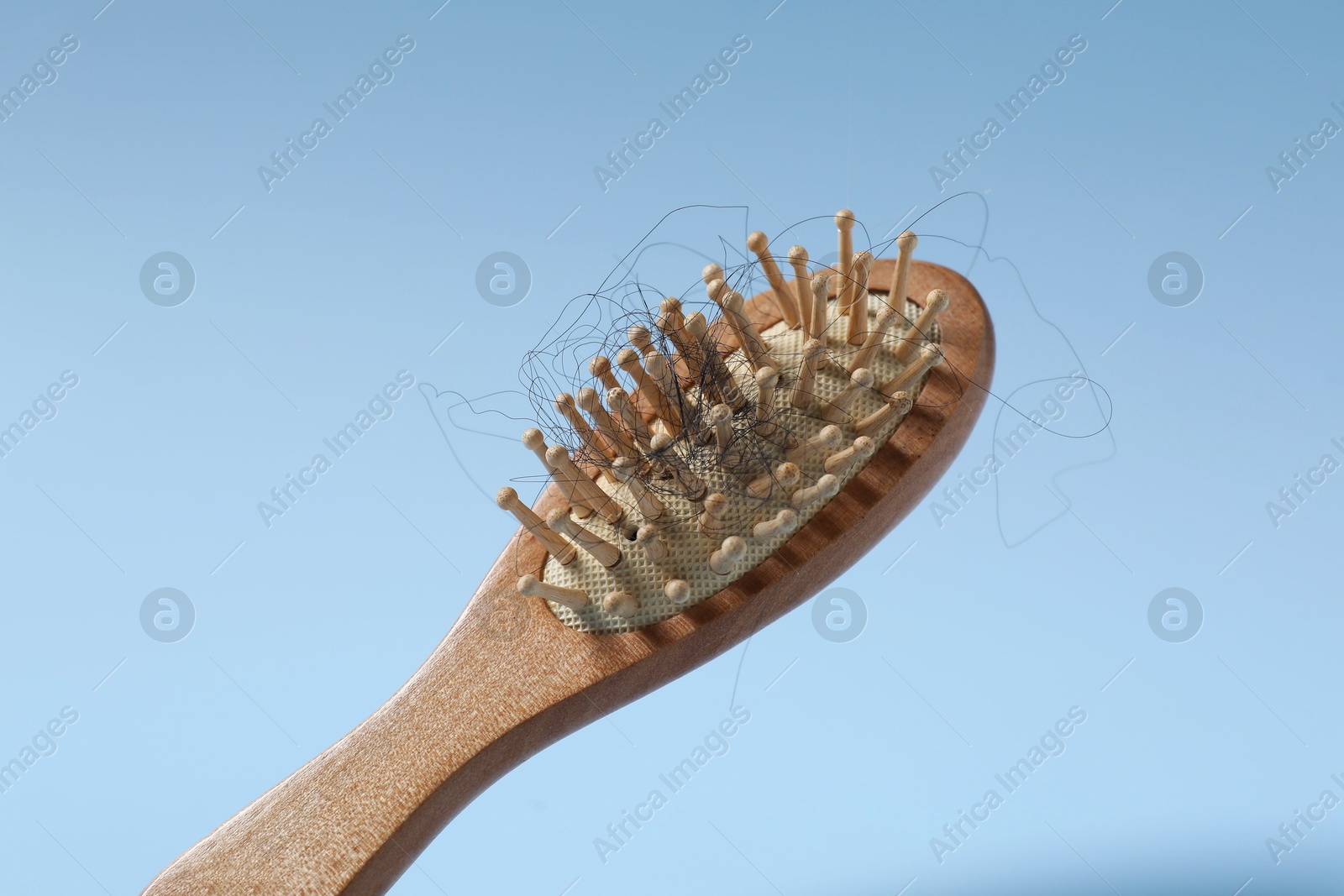 Photo of Wooden brush with lost hair in air on light blue background