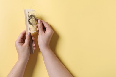 Photo of Woman taking her lost hair from comb on yellow background, top view. Space for text