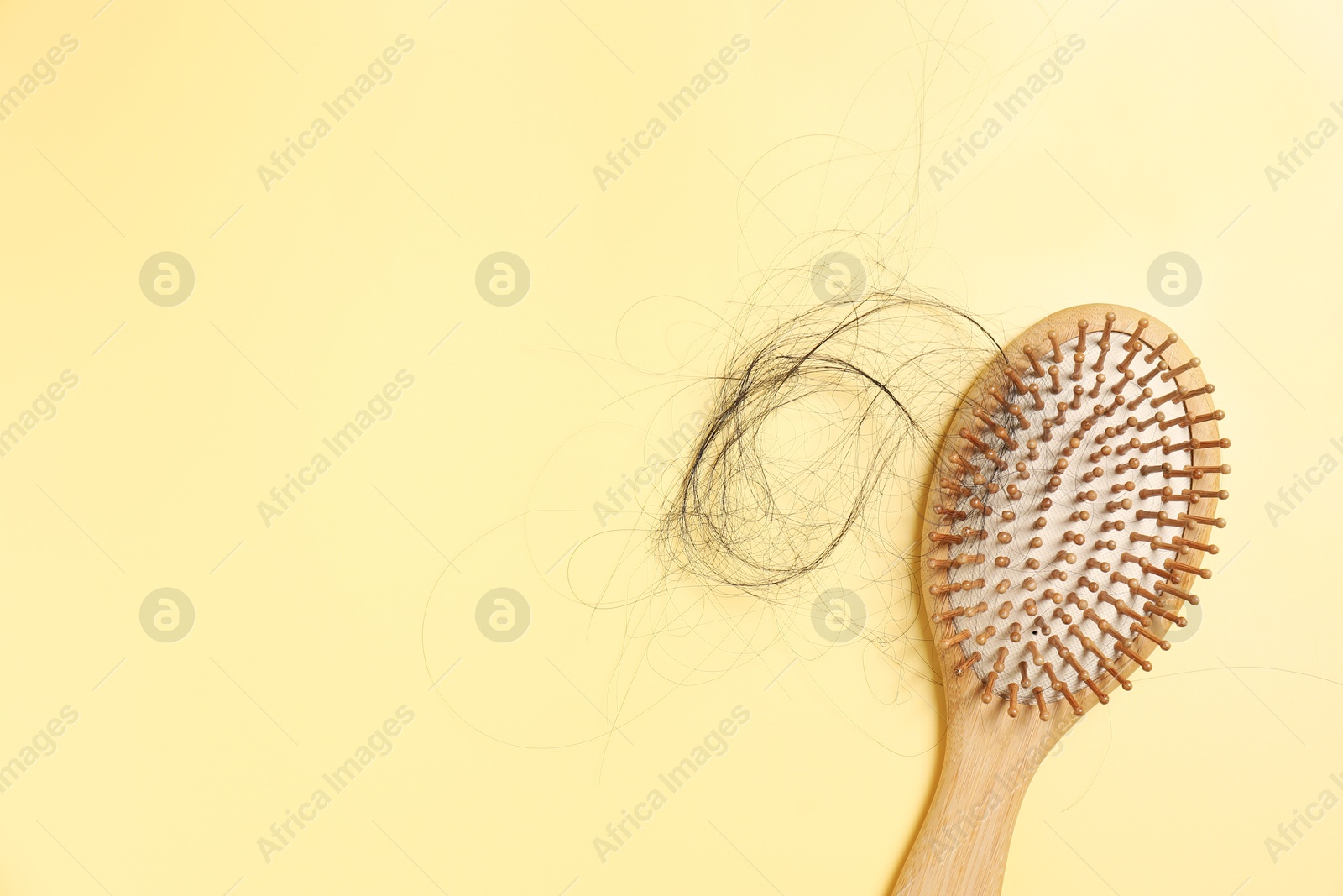 Photo of Wooden brush with lost hair on yellow background, top view. Space for text