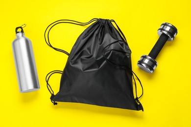 Photo of Black drawstring bag, thermo bottle and dumbbell on yellow background, flat lay