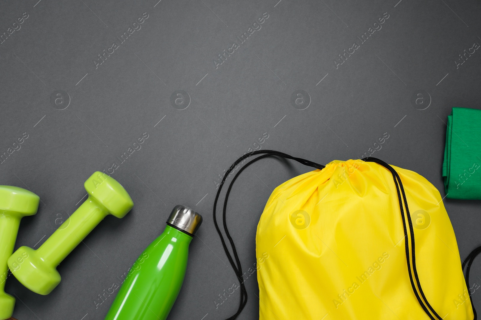 Photo of Yellow drawstring bag, thermo bottle and dumbbells on grey background, flat lay. Space for text