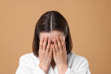 Photo of Woman suffering from hair loss problem on light brown background