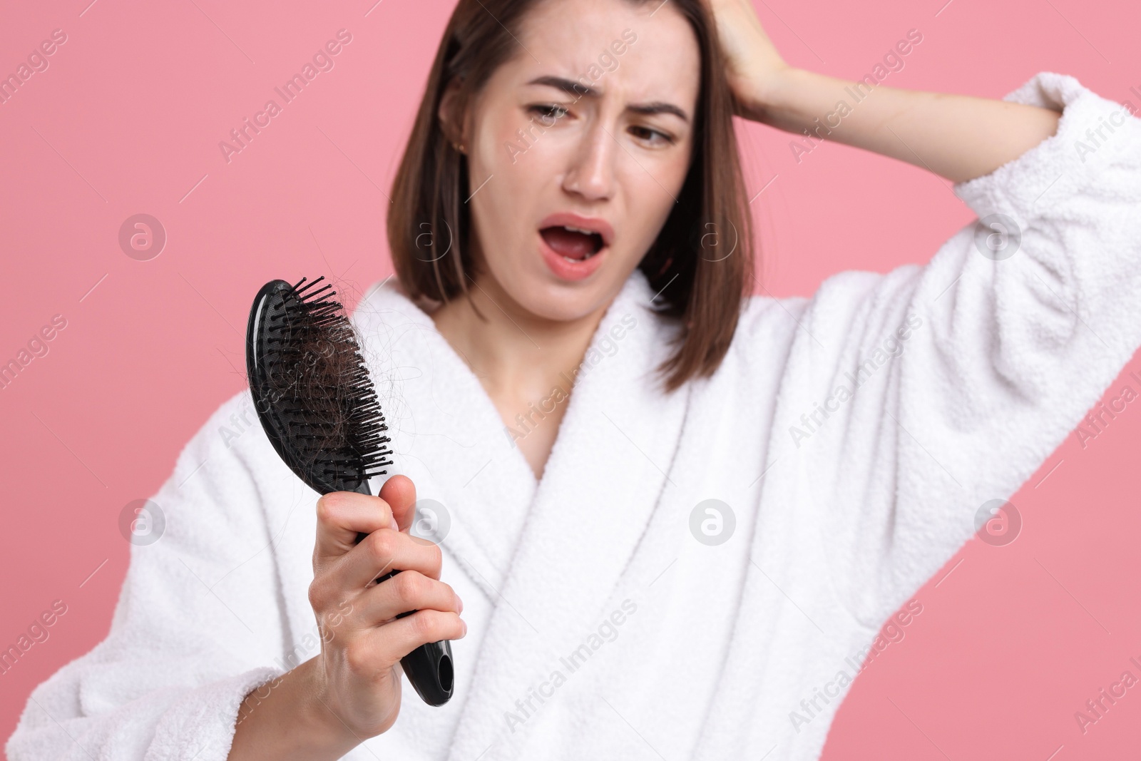 Photo of Emotional woman holding brush with lost hair on pink background, selective focus. Alopecia problem