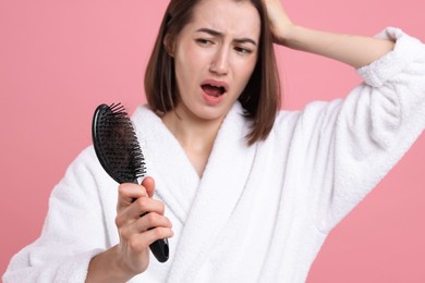 Photo of Emotional woman holding brush with lost hair on pink background, selective focus. Alopecia problem