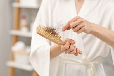 Photo of Woman taking her lost hair from brush at home, closeup. Alopecia problem