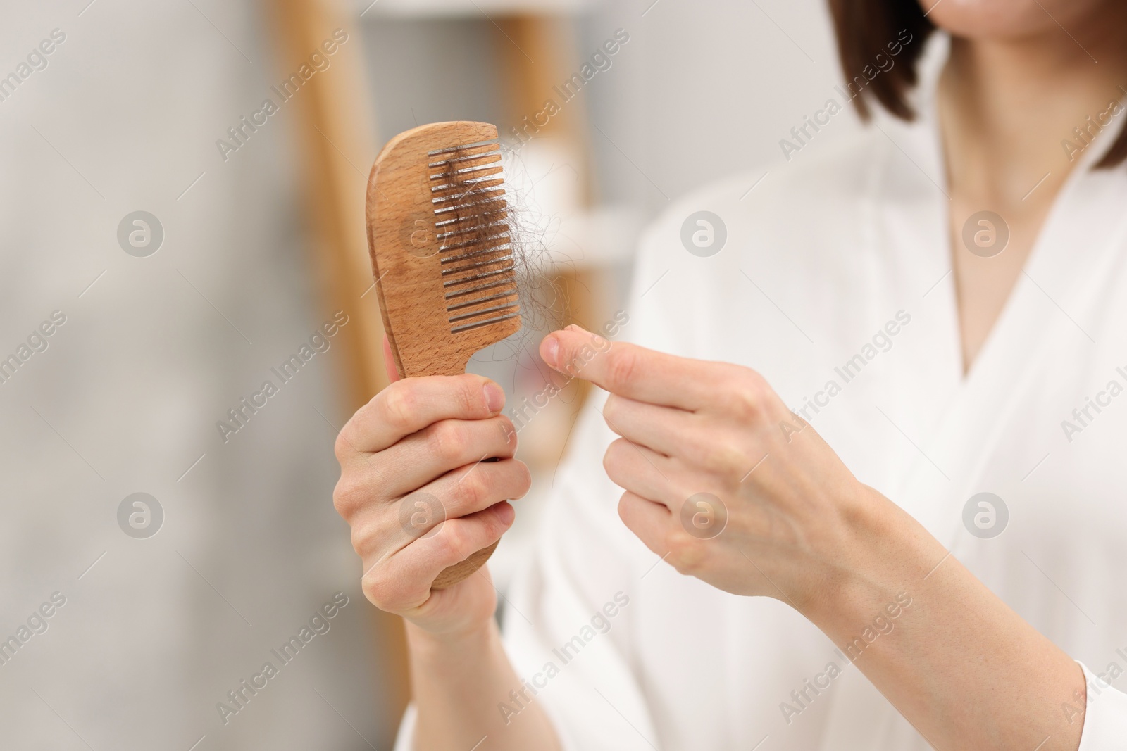 Photo of Woman taking her lost hair from comb at home, closeup. Alopecia problem