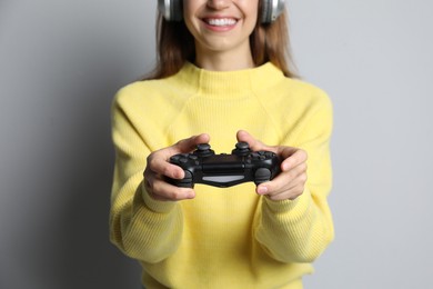 Photo of Smiling woman in headphones playing video game with controller on light grey background, closeup