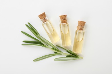 Bottles of essential oil and fresh rosemary on white background, flat lay