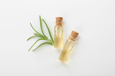 Photo of Bottles of essential oil and fresh rosemary on white background, flat lay