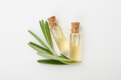 Photo of Bottles of essential oil and fresh rosemary on white background, flat lay