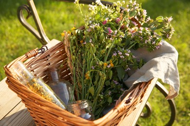 Tincture and different flowers in wicker basket on wooden bench outdoors, closeup