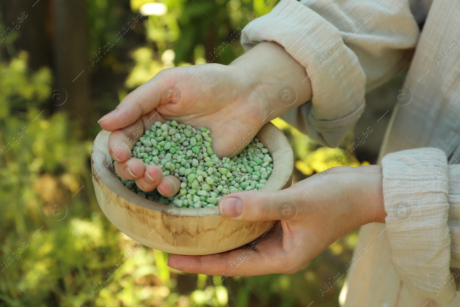 Photo of Woman holding plant fertilizer in bowl outdoors, closeup