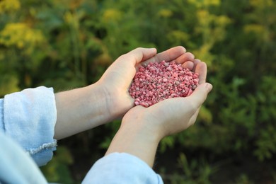 Photo of Woman holding pink plant fertilizer outdoors, closeup