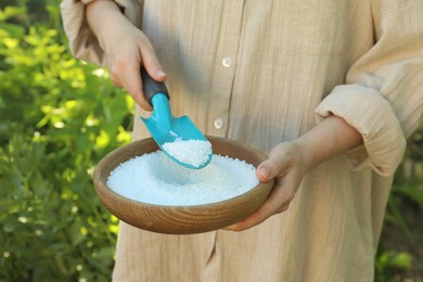 Woman holding plant fertilizer in bowl outdoors, closeup