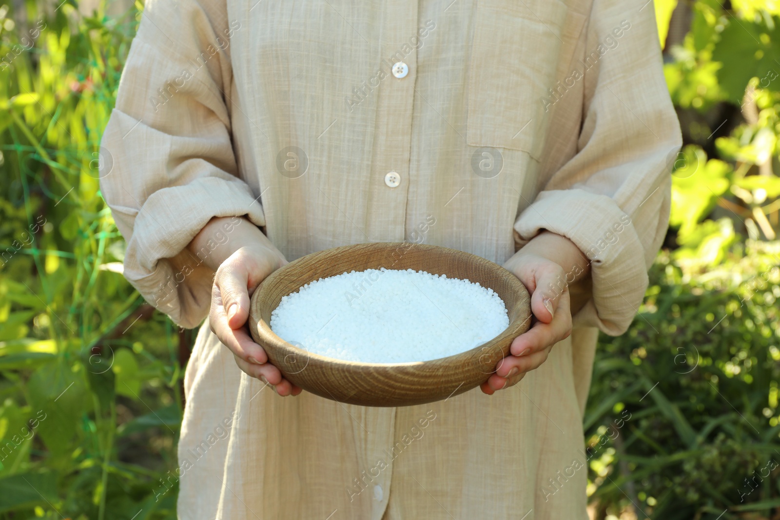 Photo of Woman holding plant fertilizer in bowl outdoors, closeup