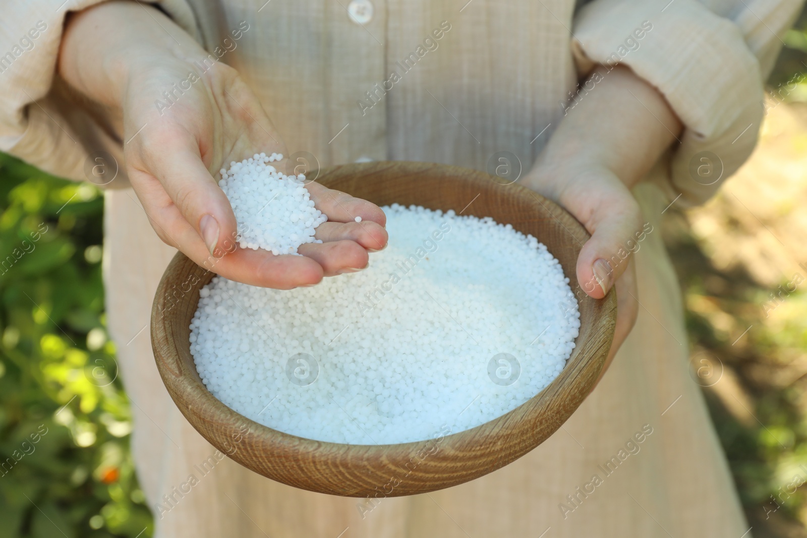 Photo of Woman holding plant fertilizer in bowl outdoors, closeup