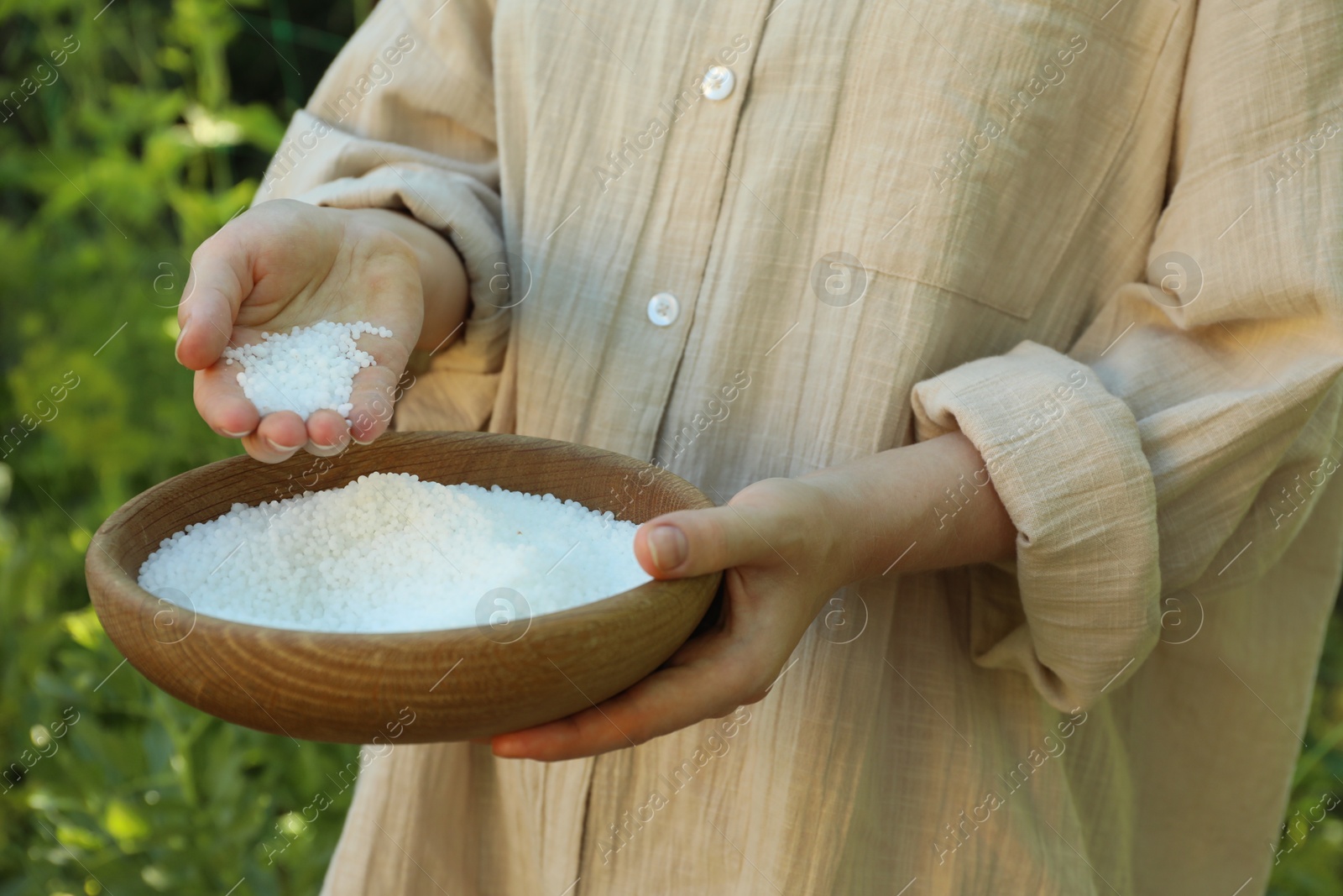 Photo of Woman holding plant fertilizer in bowl outdoors, closeup