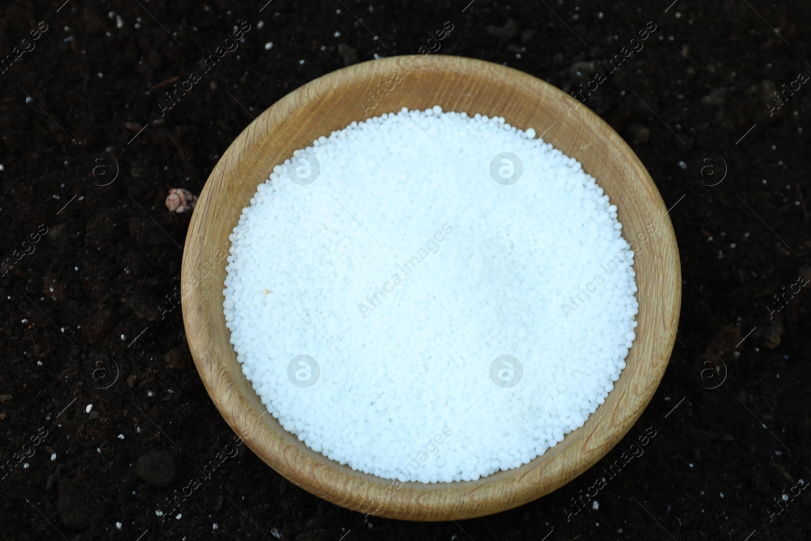 Photo of Plant fertilizer in bowl on soil outdoors, above view